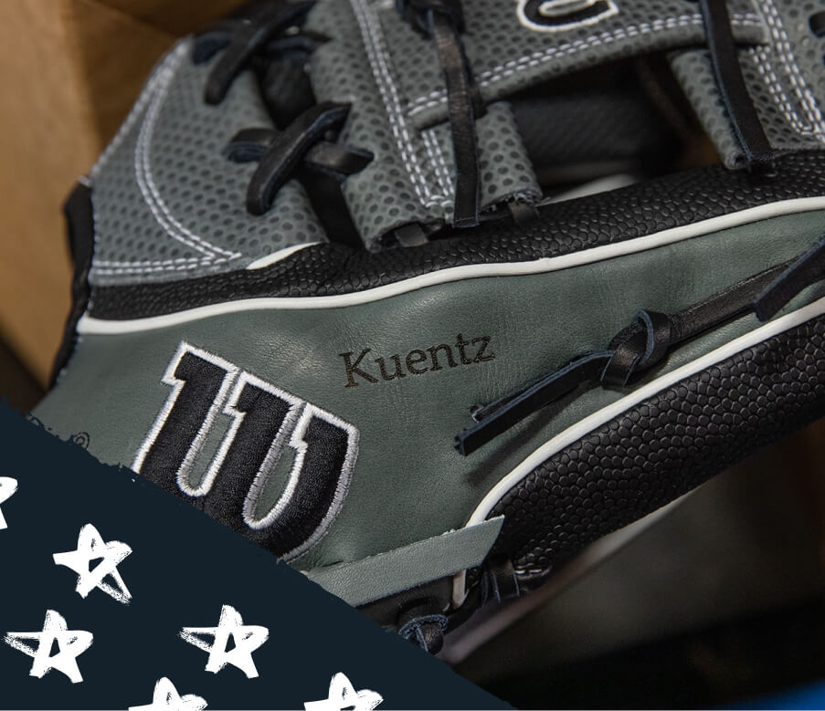 A personalized Wilson glove is engraved with the name 'Kuentz' across the thumb panel