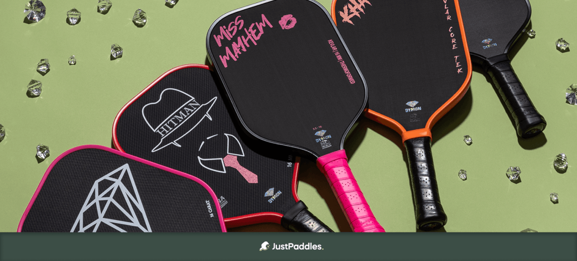 Several pickleball paddles are displayed on a light green background with scattered crystals. Visible text includes "HITMAN," "MISS MAYHEM," "KEVLAR," and "DYMON."