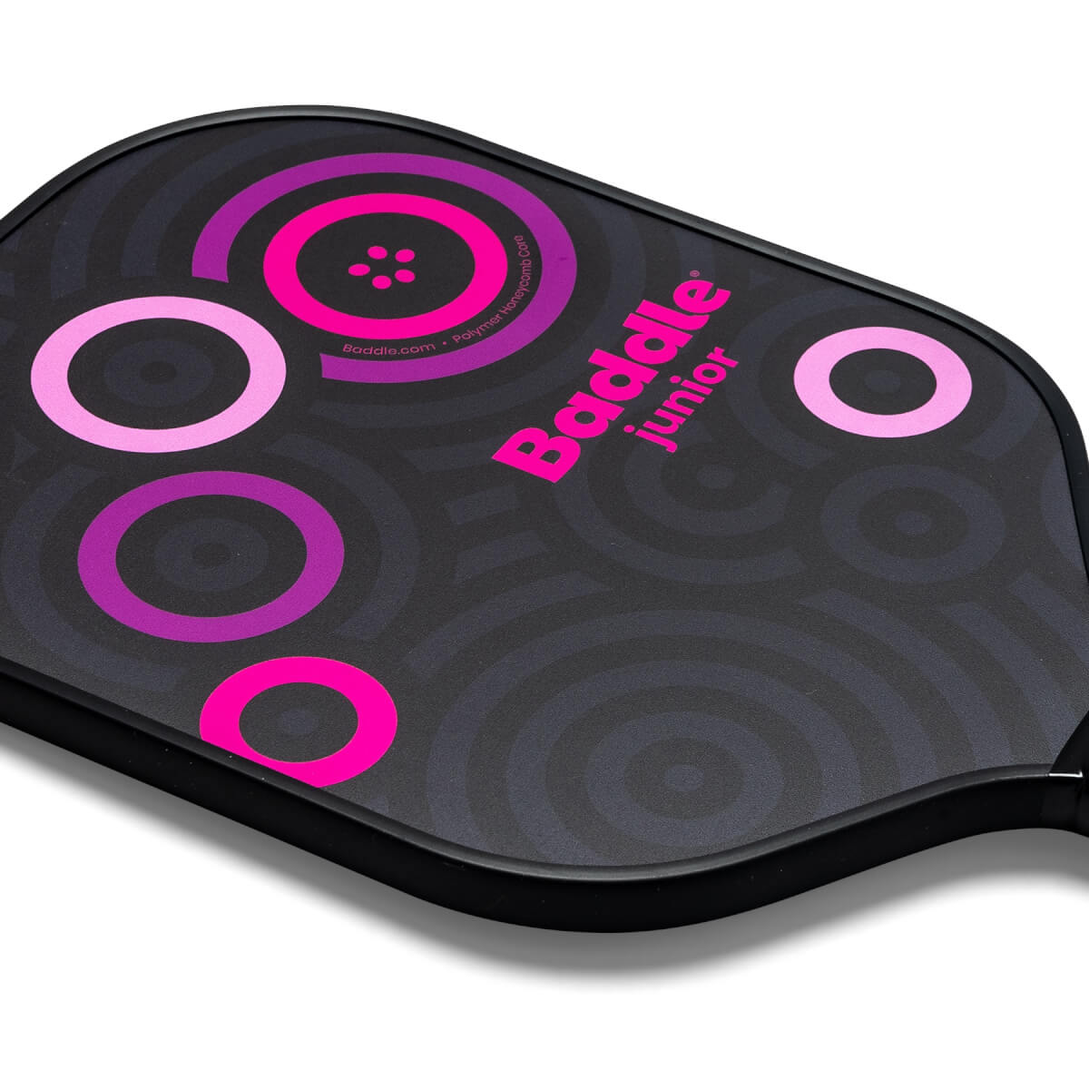 Corner view of a black Baddle Junior pickleball paddle with pink and purple concentric circles and text.