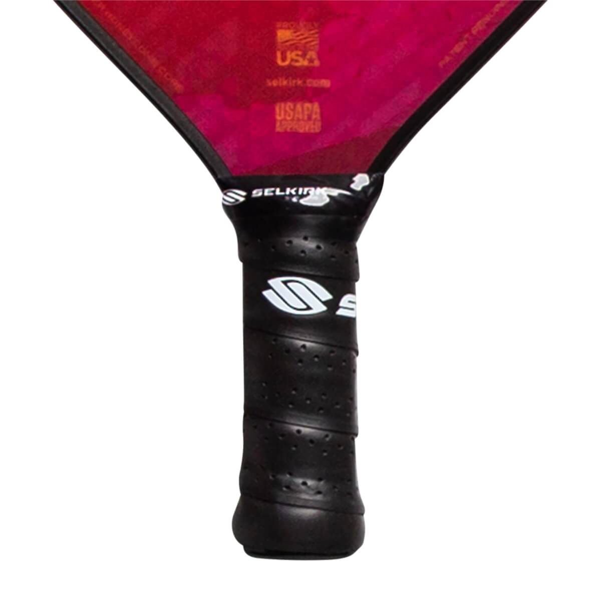 Close-up of a black pickleball paddle grip with white Selkirk logo and USAPA Approved text on the red paddle head.