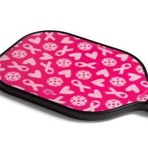 Corner view of a pink pickleball paddle with a pattern of white ribbons, hearts, and pickleballs.