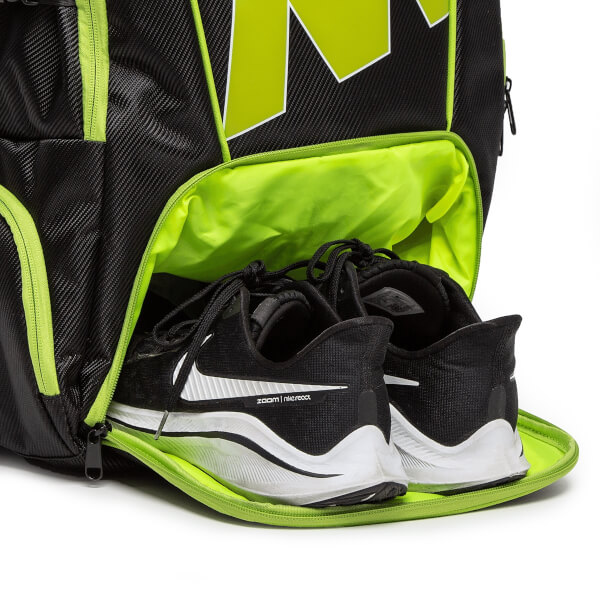 Close-up of a black pickleball backpack with neon green lining and a pair of black Nike shoes with white swooshes.