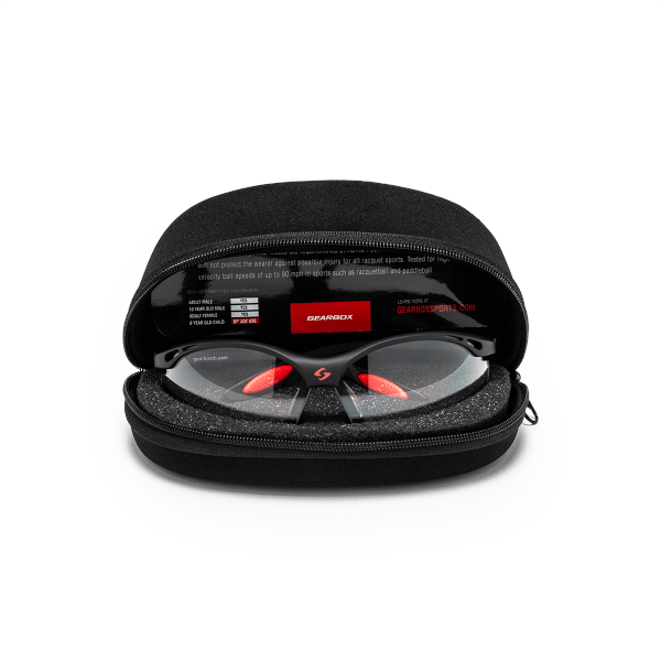 Front view of black sports glasses with red nose pads and orange accents inside a black protective case, showing the "GEARBOX" logo.
