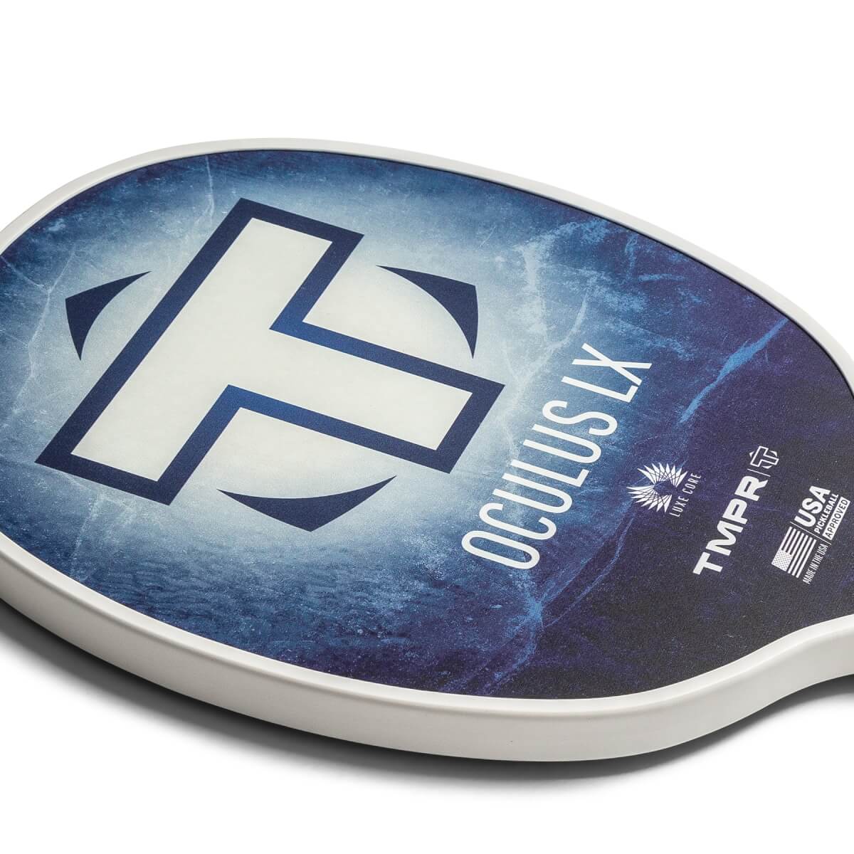 Close-up of a white pickleball paddle with a blue abstract design, white T logo, and OCULUS LX text.