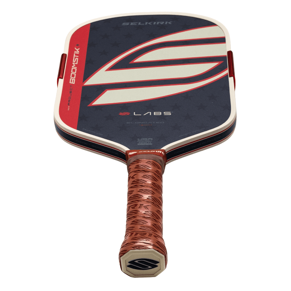 Angled bottom-up view of a Selkirk Project Boomstik Labs paddle with a navy blue star-patterned face, a large white and red S logo, and a brown textured grip.
