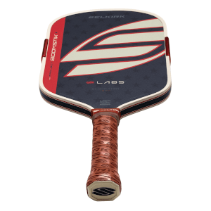 Angled bottom-up view of a Selkirk Project Boomstik Labs paddle with a navy blue star-patterned face, a large white and red S logo, and a brown textured grip.