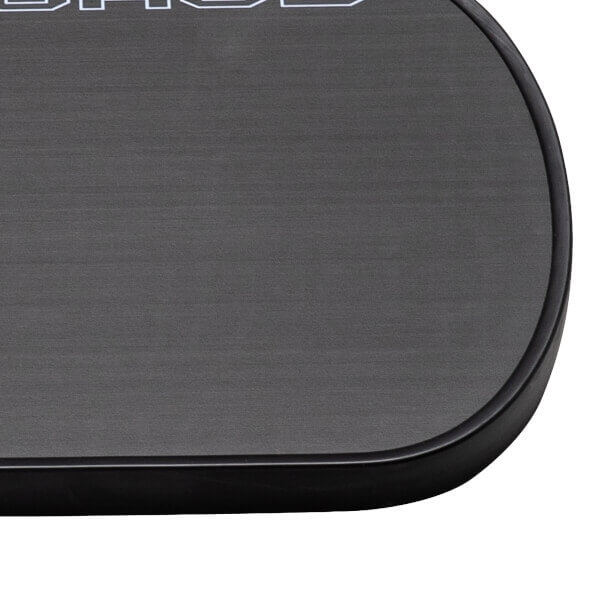 Close-up of a dark gray pickleball paddle with a textured surface, a black edge guard, and partial white lettering.