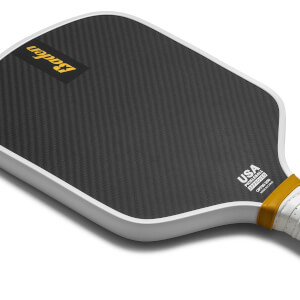 Corner view of a black pickleball paddle with a carbon fiber surface, USA Pickleball Approved logo, and yellow grip accent.