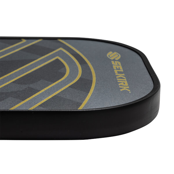 Corner view of a gray pickleball paddle with a black edge and gold Selkirk logo.