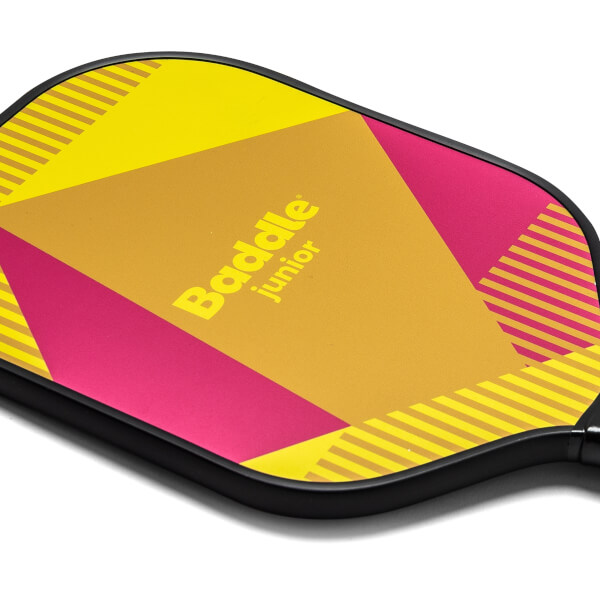 Close-up of a yellow and pink Baddle Junior pickleball paddle with geometric patterns and diagonal stripes.
