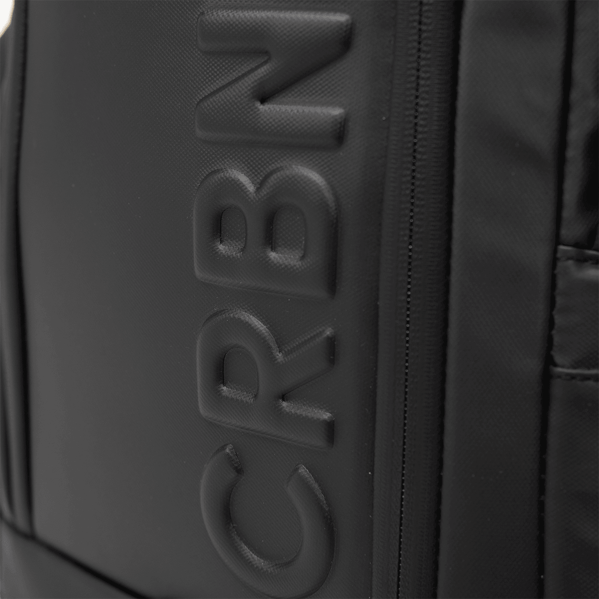Close-up of the CRBN logo embossed on the side of the black pickleball backpack.
