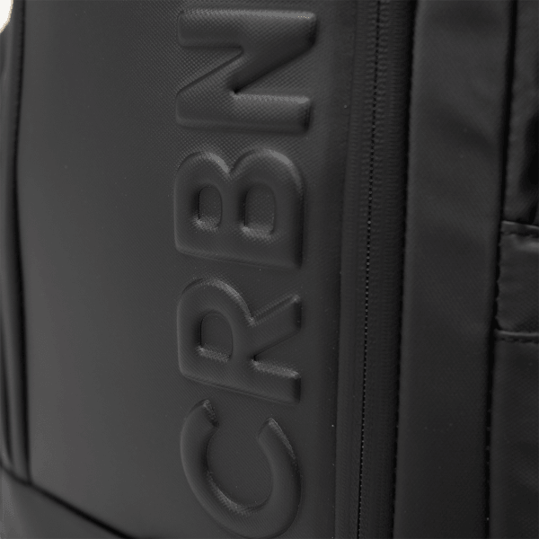 Close-up of the CRBN logo embossed on the side of the black pickleball backpack.