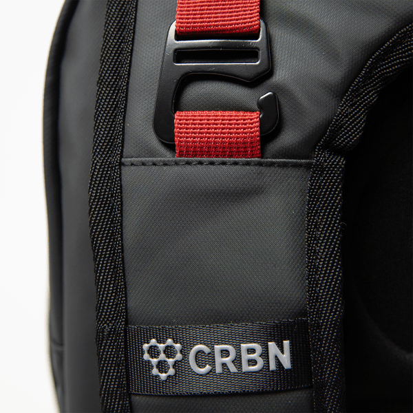 Close-up of a black bag shows a red strap with a black buckle, and a silver "CRBN" logo.