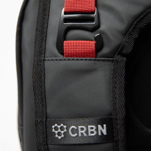 Close-up of a black bag shows a red strap with a black buckle, and a silver "CRBN" logo.