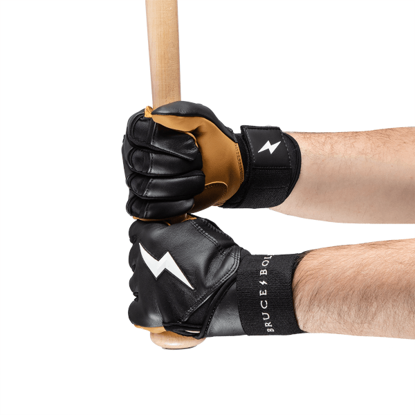 Close-up view of hands gripping a baseball bat wearing black and tan batting gloves with white lightning bolt logos and "BRUCE BOLT" text.