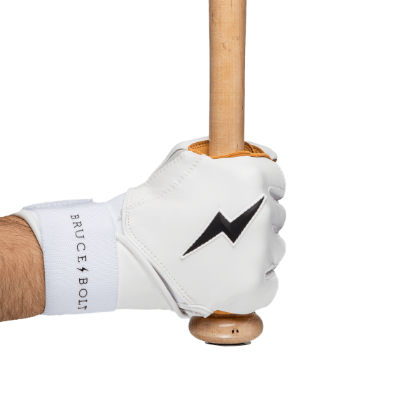 Side view of a white batting glove with a black lightning bolt logo and "BRUCE BOLT" text on a white wrist strap, gripping a wooden baseball bat.