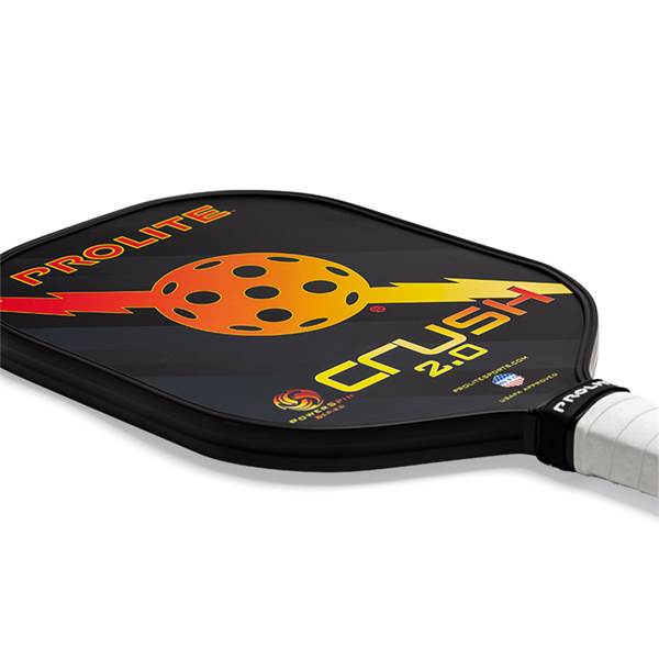 Corner view of a black pickleball paddle with PROLITE and CRUSH 2.0 text, and a circular orange and yellow graphic.