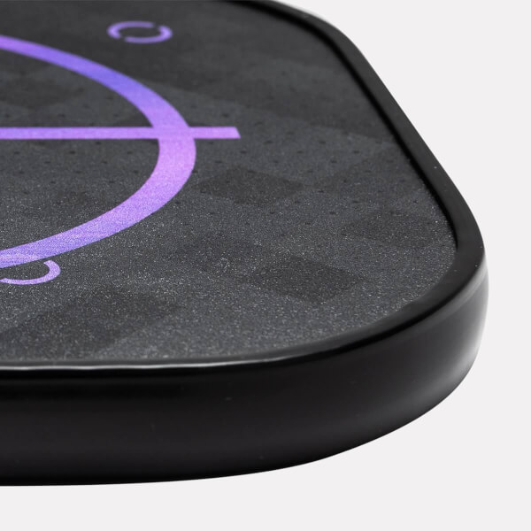 Corner view of a black pickleball paddle with a purple target design and textured surface.
