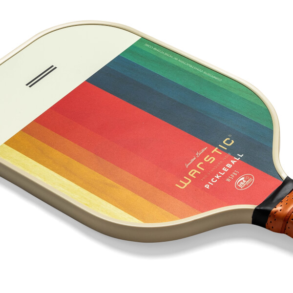 Corner view of a cream pickleball paddle with a rainbow stripe design and Warstic branding.