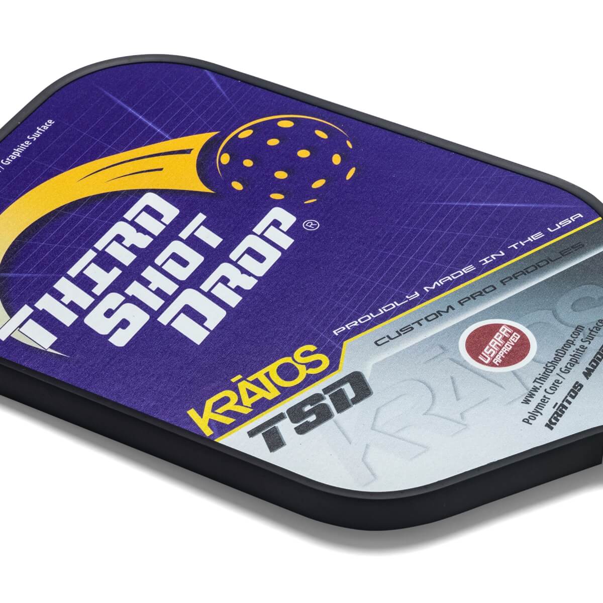 Corner view of a purple pickleball paddle with THIRD SHOT DROP text, a yellow pickleball graphic, and KRATOS TSD branding.