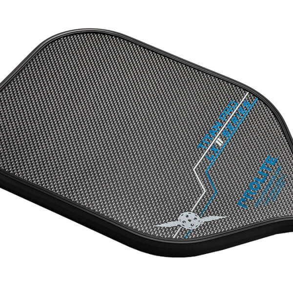Corner view of a black pickleball paddle with a carbon fiber texture, blue TITAN PRO LX text, and a winged pickleball logo.