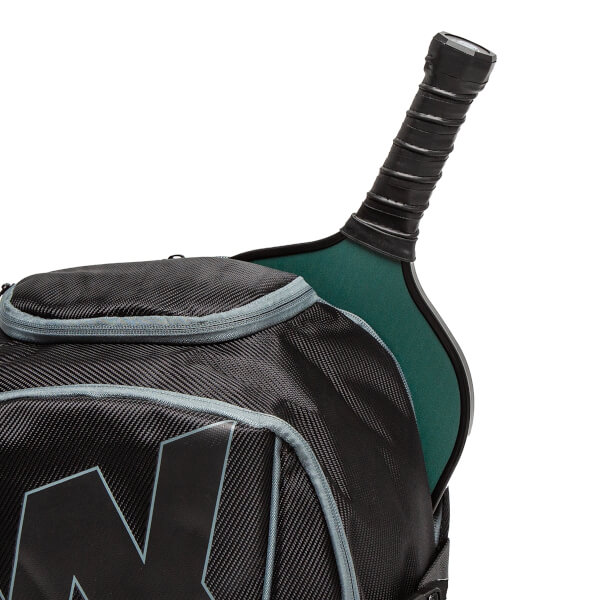 Close-up of a black pickleball backpack with a carbon fiber texture and a green pickleball paddle handle.