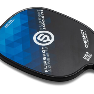Top-down view of a black pickleball paddle with blue geometric design, FLIPSHOT text, and USA PICKLEBALL APPROVED stamp.