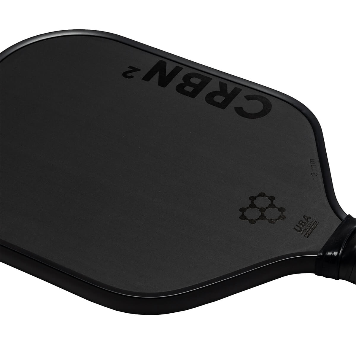 Corner view of a black pickleball paddle with CRBN² branding, a honeycomb logo, and USA Pickleball Approved text.