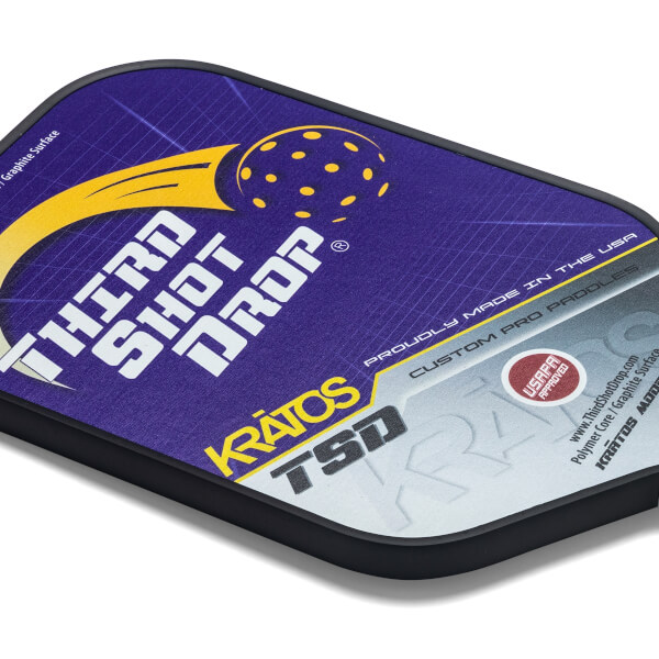 Corner view of a purple pickleball paddle with THIRD SHOT DROP text, a yellow pickleball graphic, and KRATOS TSD branding.