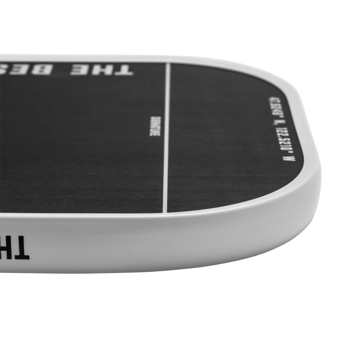 Corner view of a black pickleball paddle with white text THE BEST and coordinates.