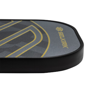 Corner view of a gray pickleball paddle with a black edge and gold Selkirk logo.