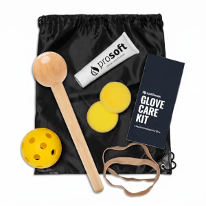 Top-down view of a black drawstring bag containing a wooden ball on a stick, a yellow ball, a tube of "prosoft" glove conditioner, and a "JustGloves. GLOVE CARE KIT" card.