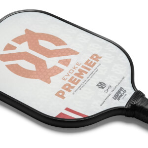 Corner view of a white pickleball paddle with a large peach logo, PREMIER text, and USAPA approved stamp.