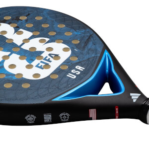 Angled close-up of a blue and black Adidas padel racket featuring gold-lined holes, a USA map graphic, and "USA" and "FIFA" text near a metallic blue bridge.