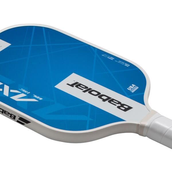 Close-up of a pickleball paddle showing the blue face with white geometric lines, the Babolat logo, and "USA PICKLEBALL APPROVED".