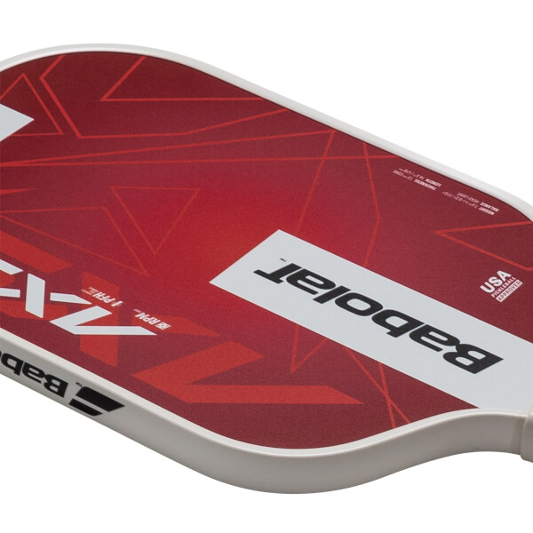 Close-up of a red pickleball paddle with white geometric patterns, "Babolat" logo, and "USA PICKLEBALL APPROVED" text.
