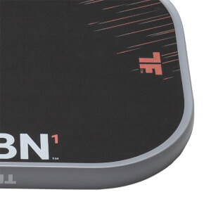 Close-up of a dark gray pickleball paddle with a textured surface, light gray edge guard, and visible CRBN¹ and TF branding.