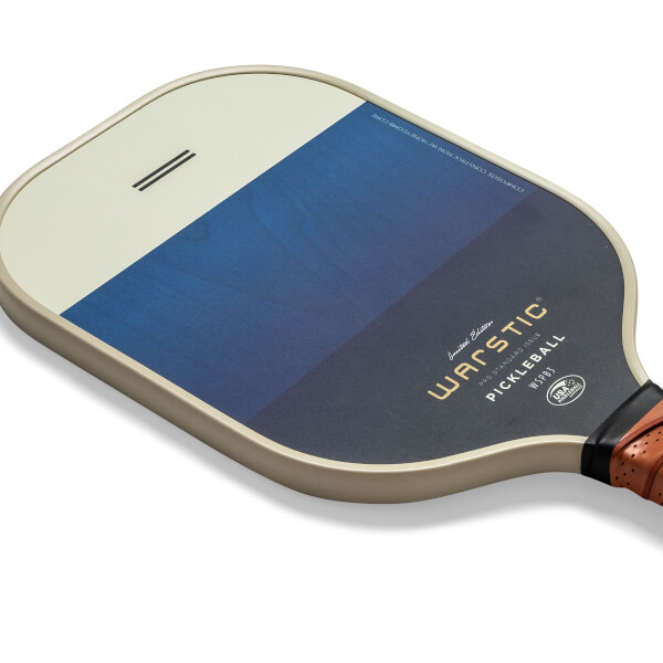 Corner view of a tan pickleball paddle with a blue gradient and Warstic branding.