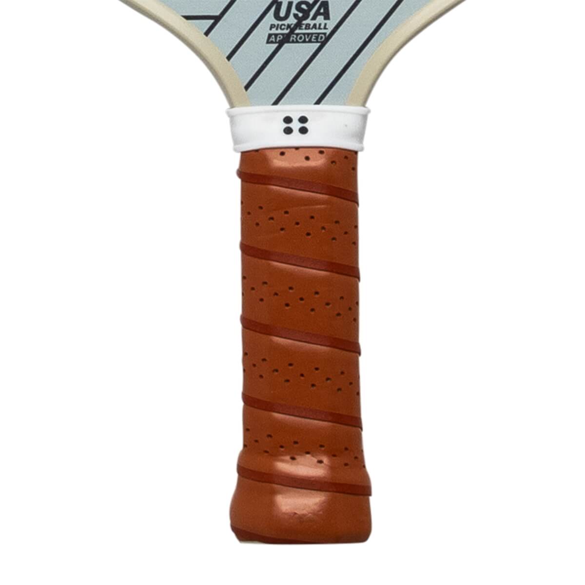 Close-up of a brown pickleball paddle grip with perforations and a white band with four dots.
