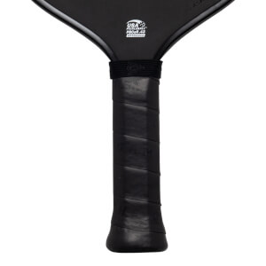 Close-up of the black paddle handle and lower face, featuring a white USA PICKLEBALL PBCoR.43 APPROVED logo and textured black grip tape.