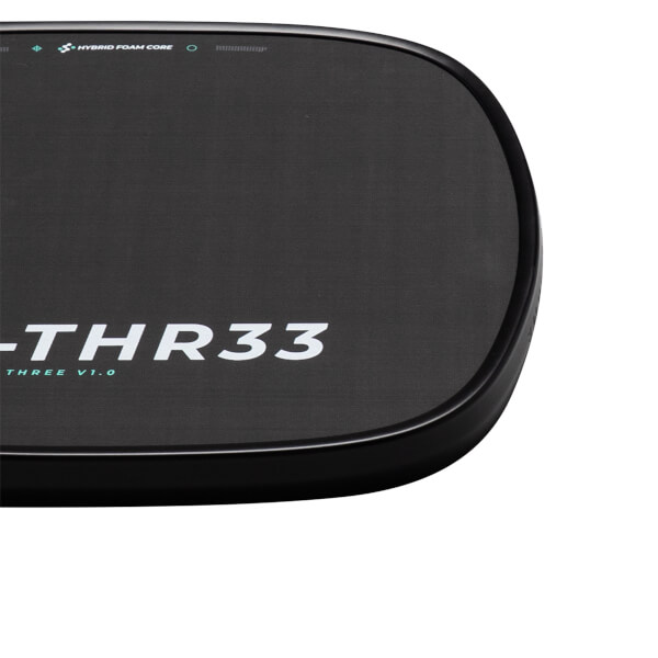 Close-up corner of the black paddle surface showing white "-THR33" text and a teal "HYBRID FOAM CORE" label along the rounded edge.