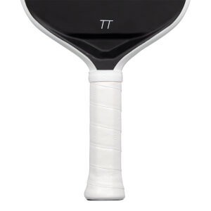 Close-up view of a paddle showing its white wrapped handle and the lower portion of its black face featuring a white TT logo.