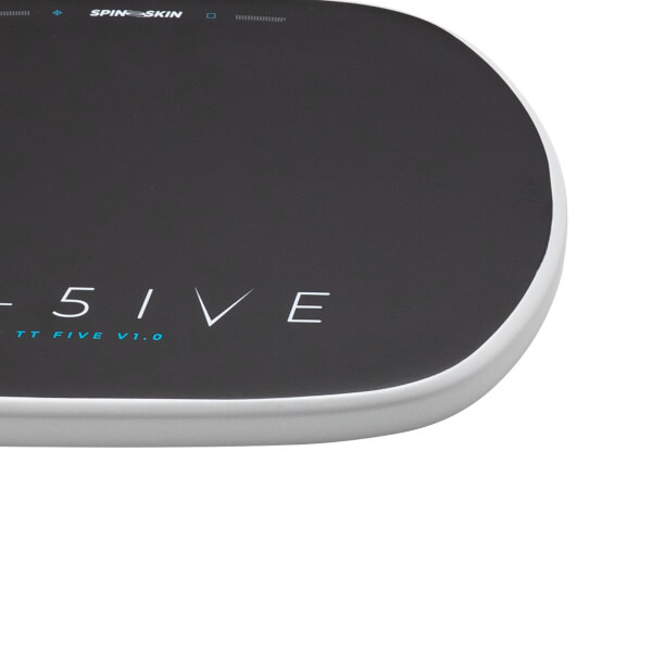 Close-up corner view of a dark textured mat with a white rounded edge, featuring SPINE SKIN, 5IVE, and TT FIVE V1.0 text on the surface.
