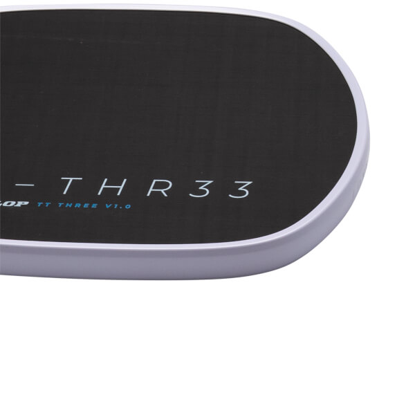 Close-up corner view of a black surface with a light-colored rim, featuring the text "THR33" in white and "TT THREE V1.0" in blue.