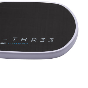 Close-up corner view of a black surface with a light-colored rim, featuring the text "THR33" in white and "TT THREE V1.0" in blue.