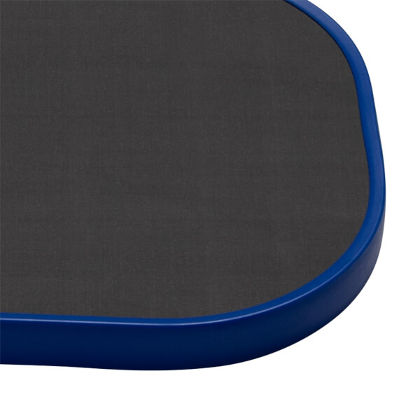 Close-up corner view of the paddle showing its dark gray textured carbon fiber face and a thick, rounded blue edge guard.