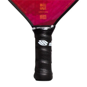 Close-up of a black pickleball paddle grip with white Selkirk logo and USAPA Approved text on the red paddle head.