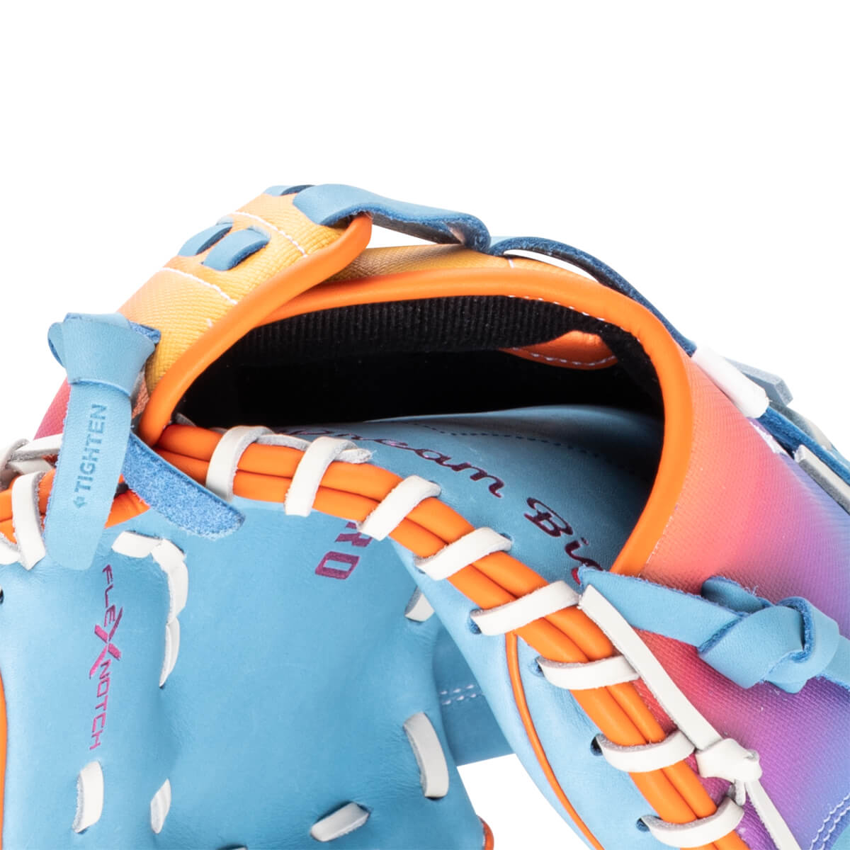 Close-up of a blue baseball glove with orange lacing, featuring "Dream Big" text and a gradient of pink and purple on the back.