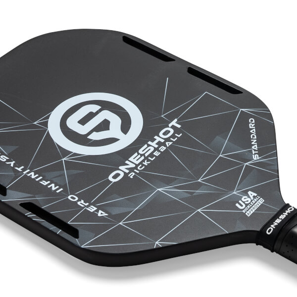 Top-down view of a black pickleball paddle with a white geometric pattern, ONESHOT PICKLEBALL text, and USA PICKLEBALL APPROVED stamp.