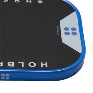 Close-up of a black pickleball paddles bottom right corner with a blue edge guard. HOLBR, ZONE, POWER text and a light blue design with four circles are visible.